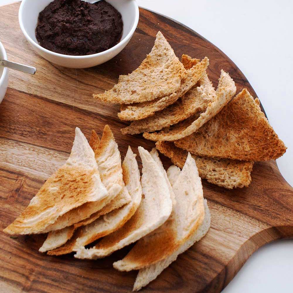 two piles of melba toast on a wooden board with dips