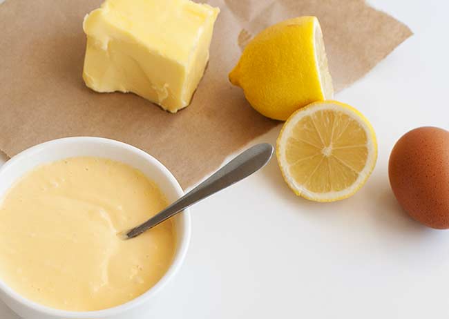 Ingredient focus - Butter, cut lemon and a whole egg sat on a paper bag with a bowl of easy hollandaise in the corner.