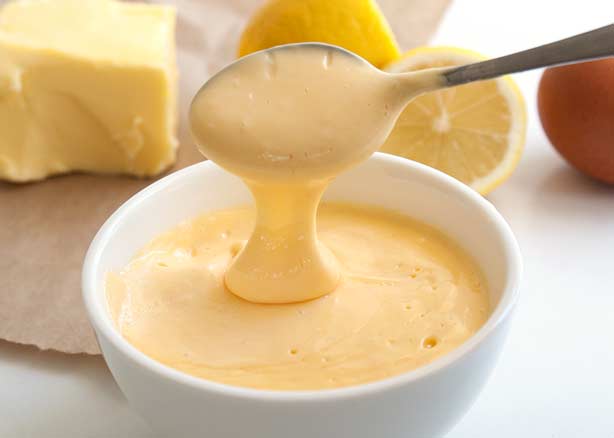 Spoon of easy hollandaise being scooped from a small white bowl.