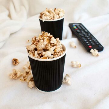 two cups of popcorn sitting on a blanket with a TV controller behind them