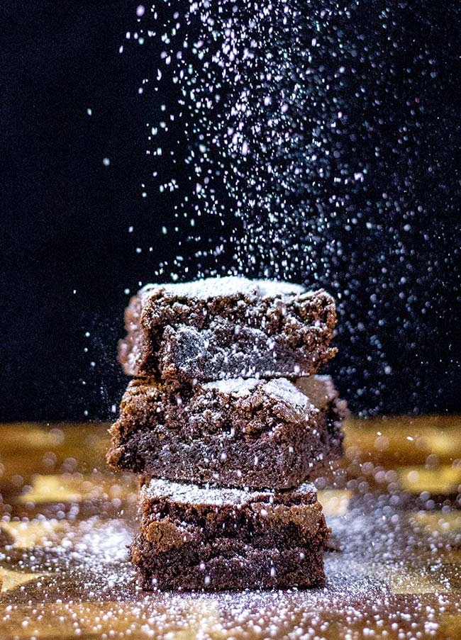 3 brownies stack on top of each other with sugar sprinkling down.