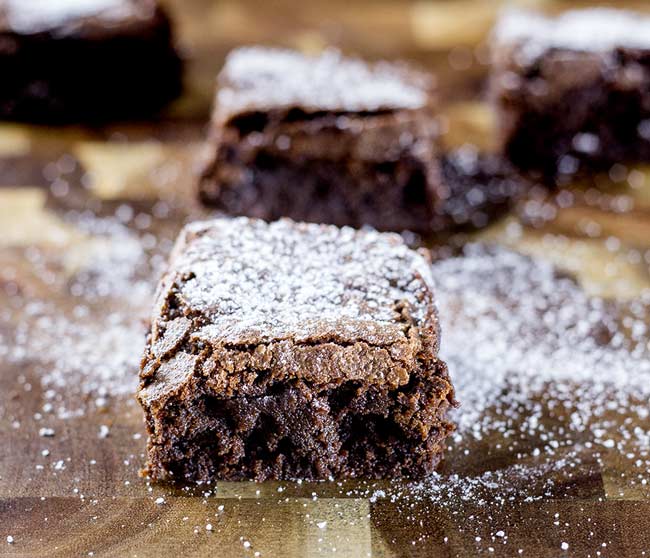 Single fudgy brownie on a wooden board sprinkled with sugar.