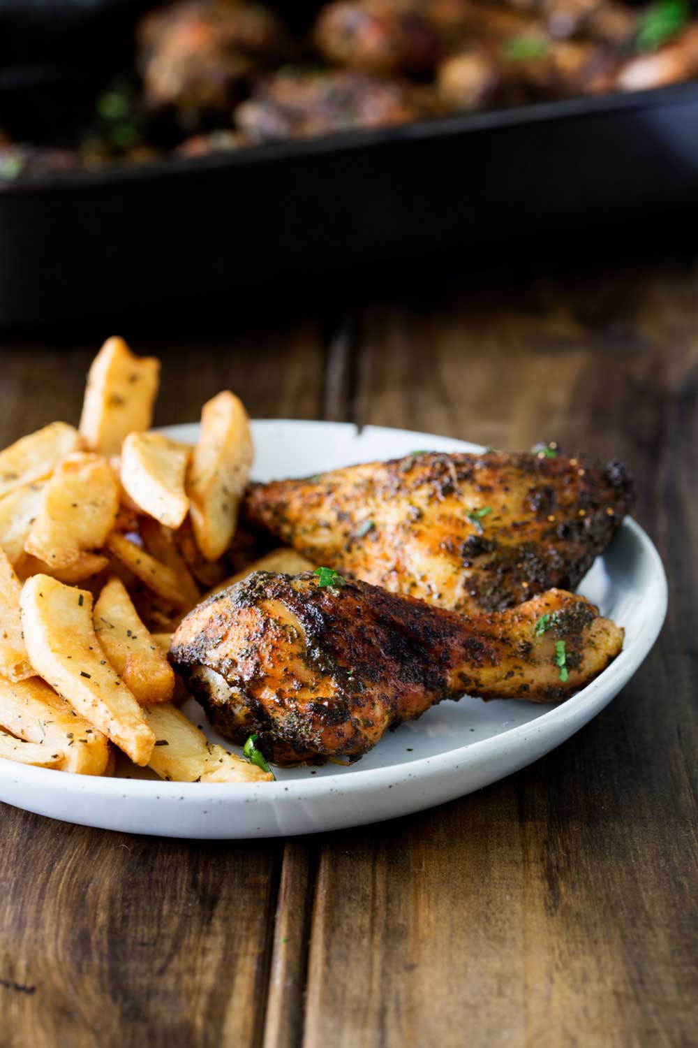 a white plate with roasted chicken pieces and french fries on a wooden table
