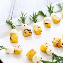 Charred pineapple, chilli mozzarella on a rosemary skewers, on a white plate.