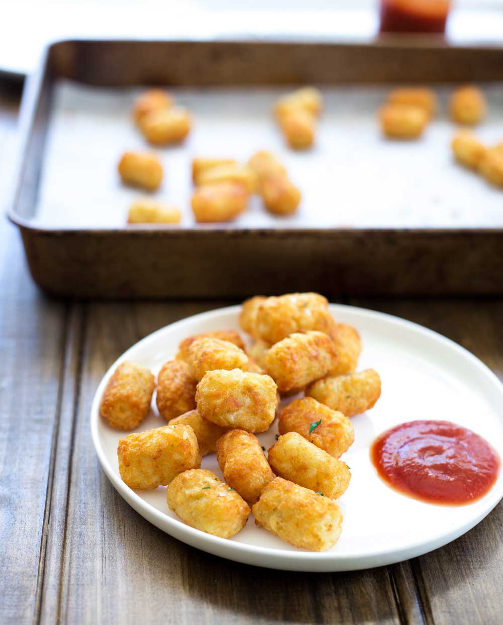 a white plate of tater tots with a. pool of tomato ketchup in the side on a wooden table