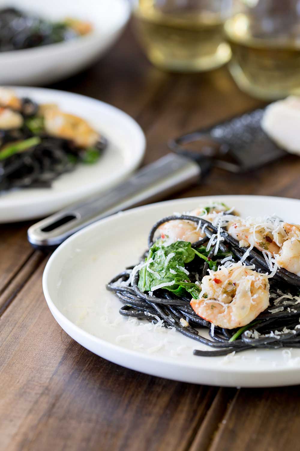 two plate of black shrimp pasta on a wooden table