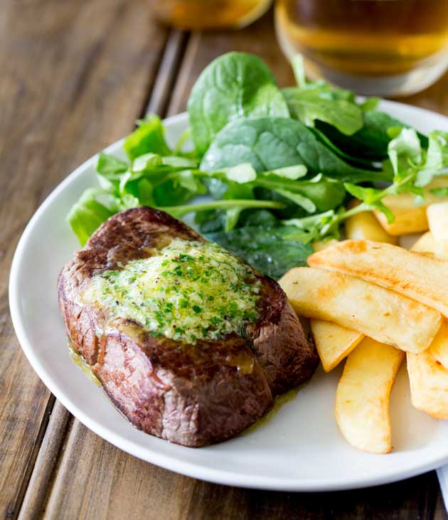 a steak with butter on top on a white plate with fries and salad