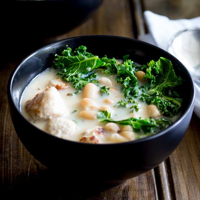 close up on a matt black soup bowl with a creamy chicken and kale soup