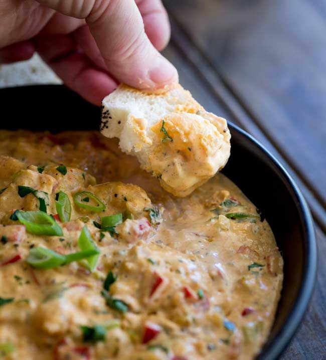 Bread being dunked into bowl of Hot Louisiana shrimp dip.