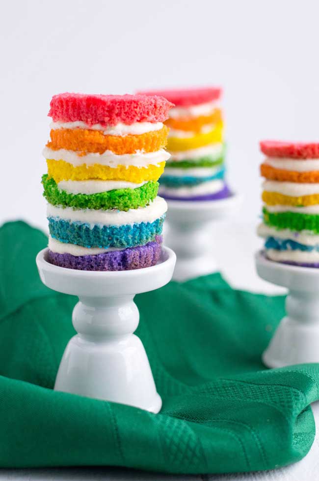 white table with green napkin and 3 mini rainbow cakes on it.