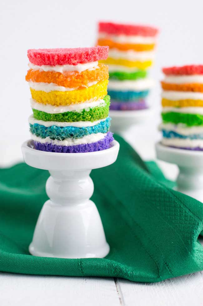 A mini 6 layer rainbow cake sat on a mini white cake stand.
