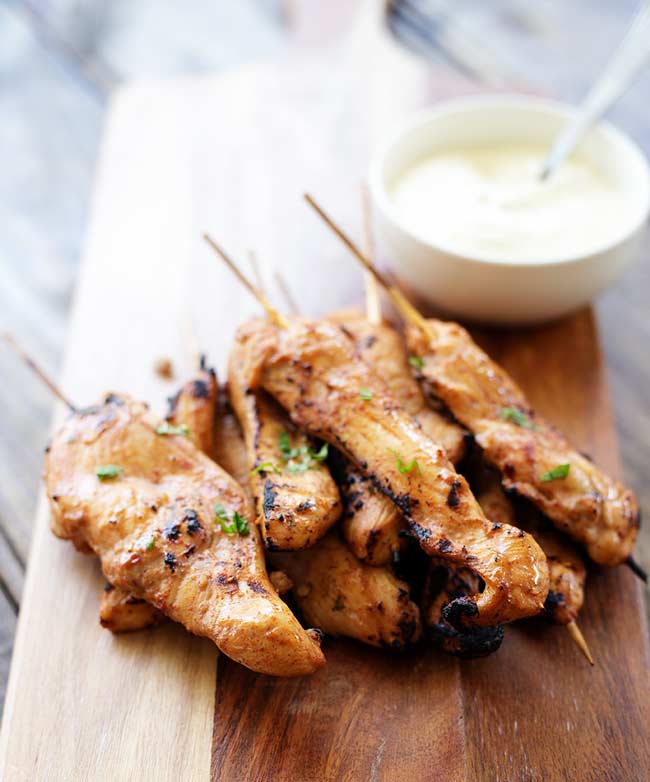 Hot and spicy chicken skewers, golden and charred from the grill, garnished with fresh parsley.