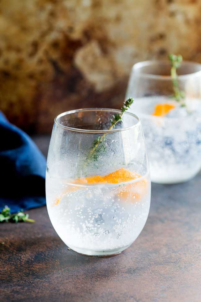 two stemless wine glasses filled with  G&T and garnished with orange zest and thyme sprig