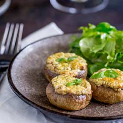 Square picture of 3 basil and cheese stuffed mushrooms on a grey plate with a side salad.