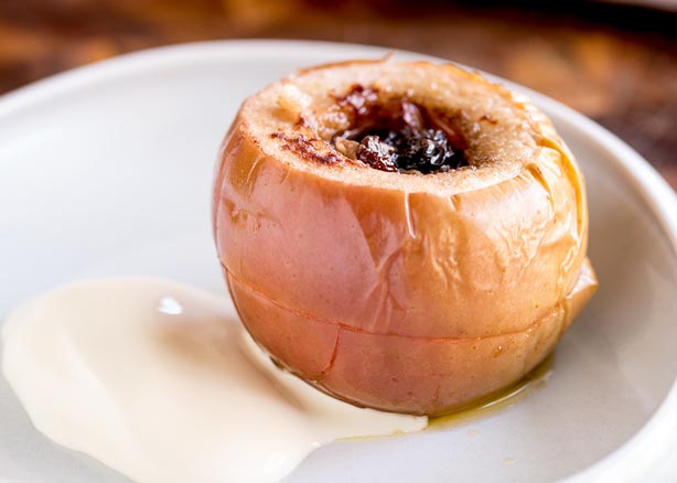 FEATURE IMAGE - Close up of a Slow Cooked Apple stuffed with Walnuts and Sultanas, served on a plate with cream.