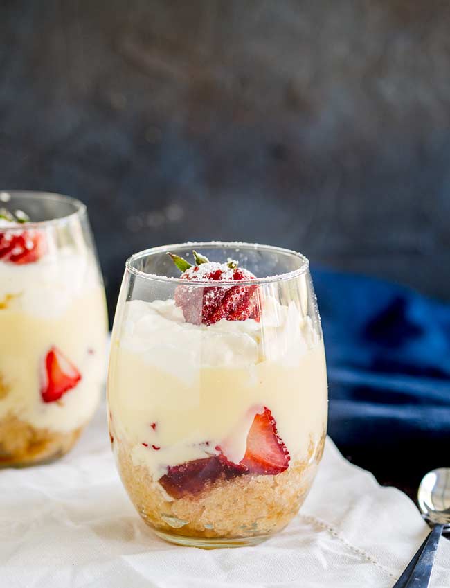 Two individual trifles in wine glasses with a blue napkin in the background.