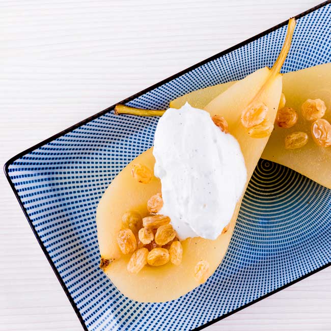 Wine poached pears with golden raisins on a blue and white plate.