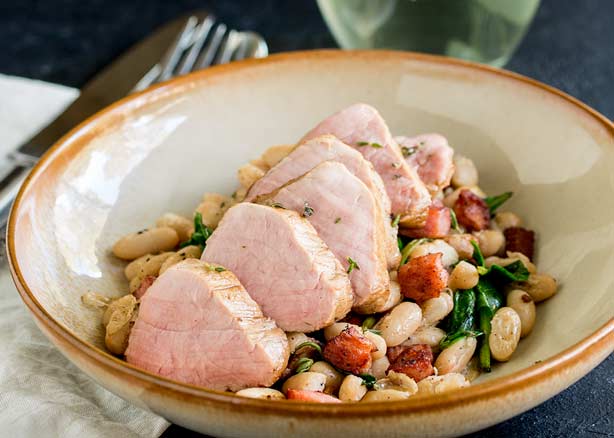 FEATURE IMAGE - Showing the whole dish of Pork tenderloin on top of a bowl of beans and bacon.