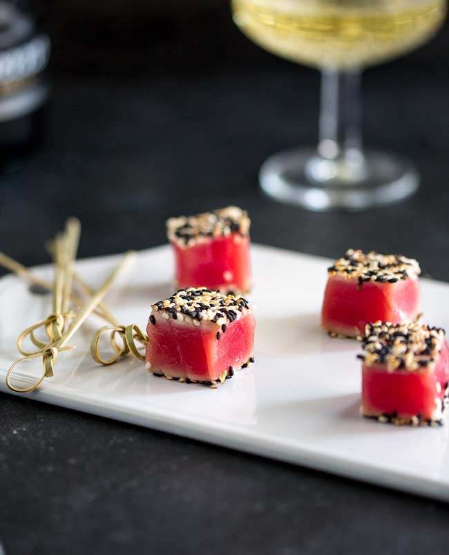 Close up of the seared sesame tuna cubes, on a white platter with champagne in the background.