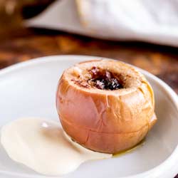 Square Close up of Slow Cooked Apple stuffed with Walnuts and Sultanas, served on a plate with cream.