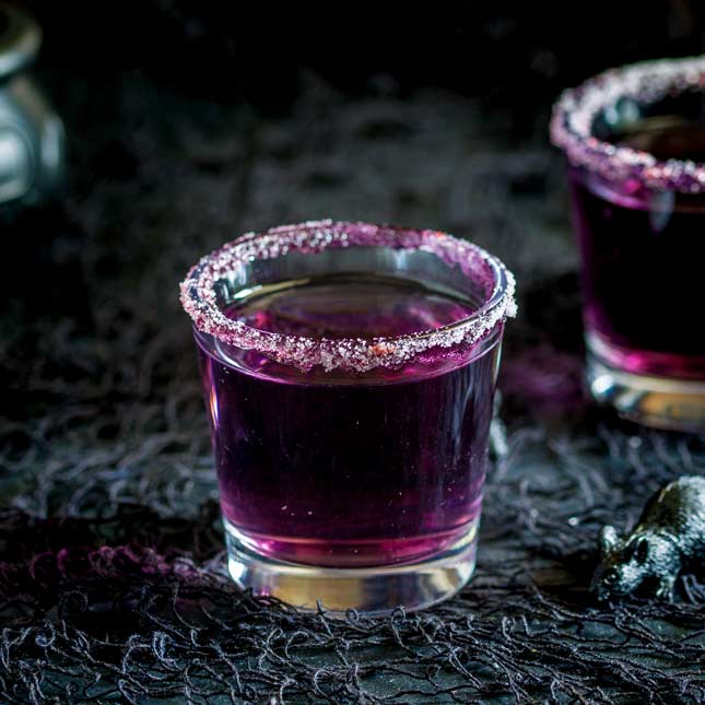 Single shot glass with a purple cocktail with a sugar rim.