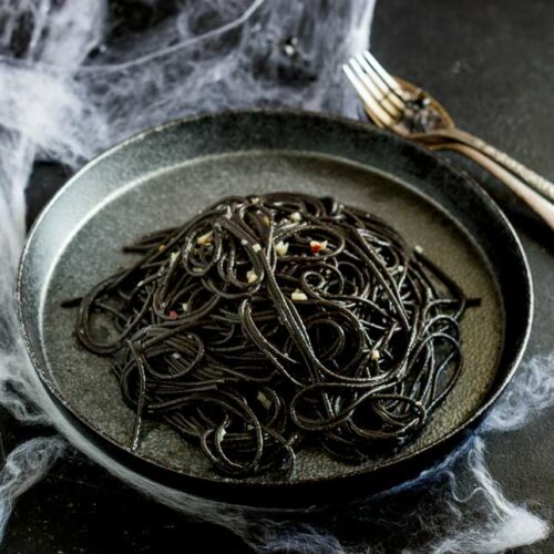 overhead showing the black pasta on a black plate with cobwebs over the table and cutlery