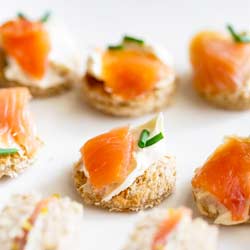 Toast rounds topped with cream cheese, chive and smoked salmon on a white plate.