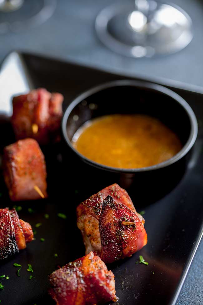 Close up on a Brown Sugar Bacon Wrapped Chicken Bites and a small black dish of mustard maple dipping sauce