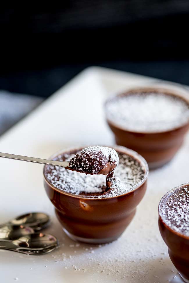 Chocolate pot, small glass pot filled with a rich chocolate mousse, sprinkled with sugar. With a spoonful taken out, showing the creamy texture.
