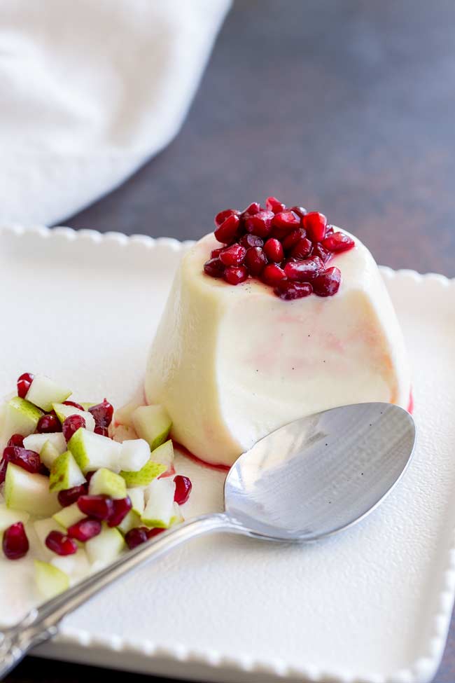 Close up version of the pear and Pomegranate panna cotta, with a silver spoon and a section missing from the panna cotta.
