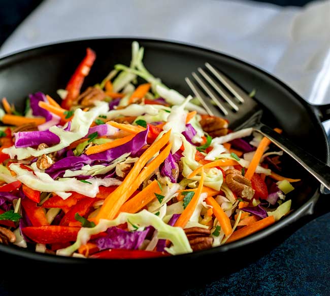 Red and white cabbage, red pepper and carrot slaw in a black bowl.