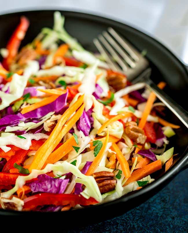 Large black bowl filled with winter slaw and a fork on the side.