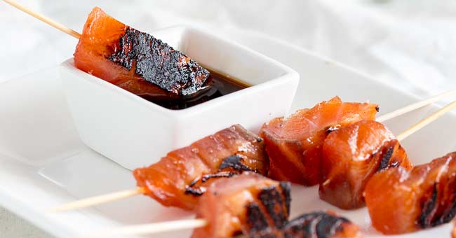 The cured Brown Sugar Salmon skewers being dipped into a white bowl of soy sauce.