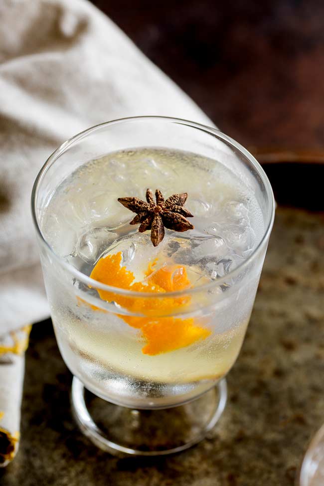 Overhead shot showing the star anise floating in the orange gin and tonic, with a linen napkin on an old metal tray