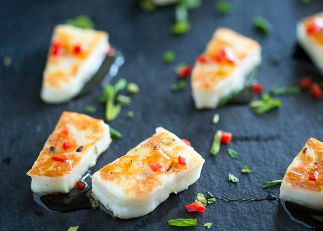 Slate platter with small bites of grilled halloumi cheese on it, flecked with red chilli and green mint