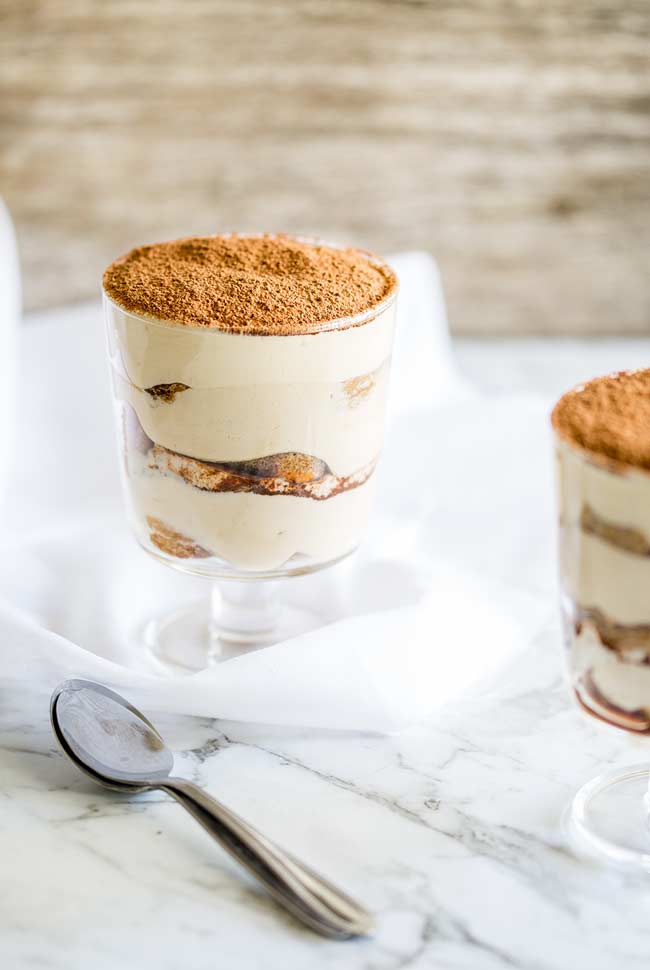 Two glasses with Tiramisu, on a marble table with white napkins and silver spoons