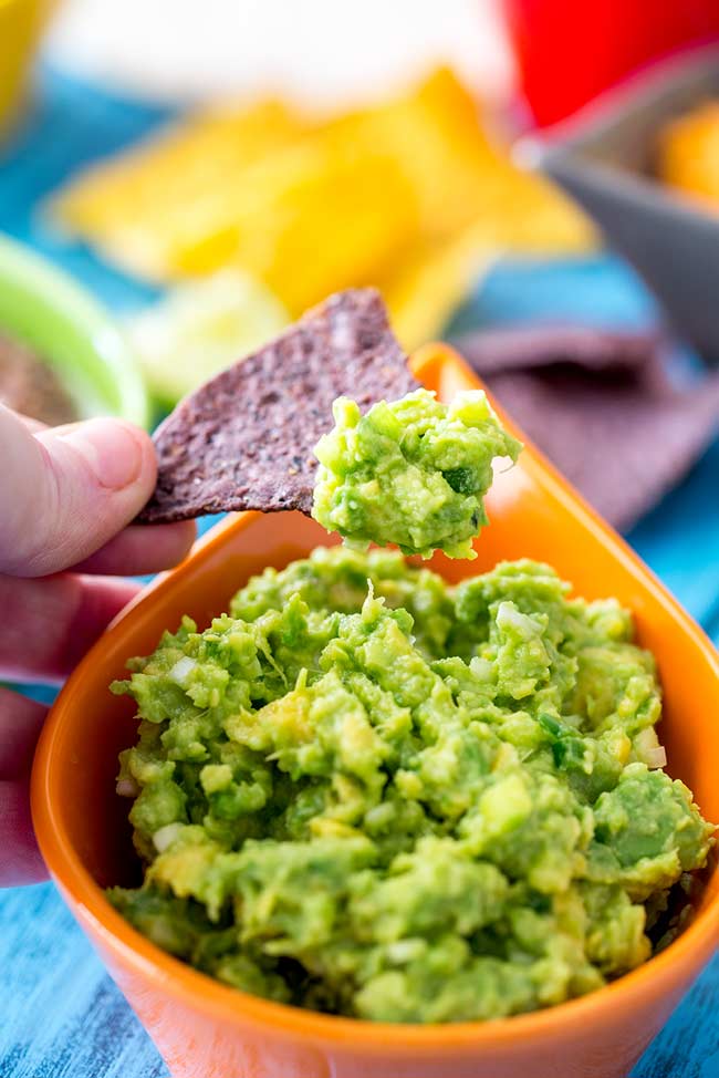 Someone scoop this stay green guacamole up with a blue corn chip.