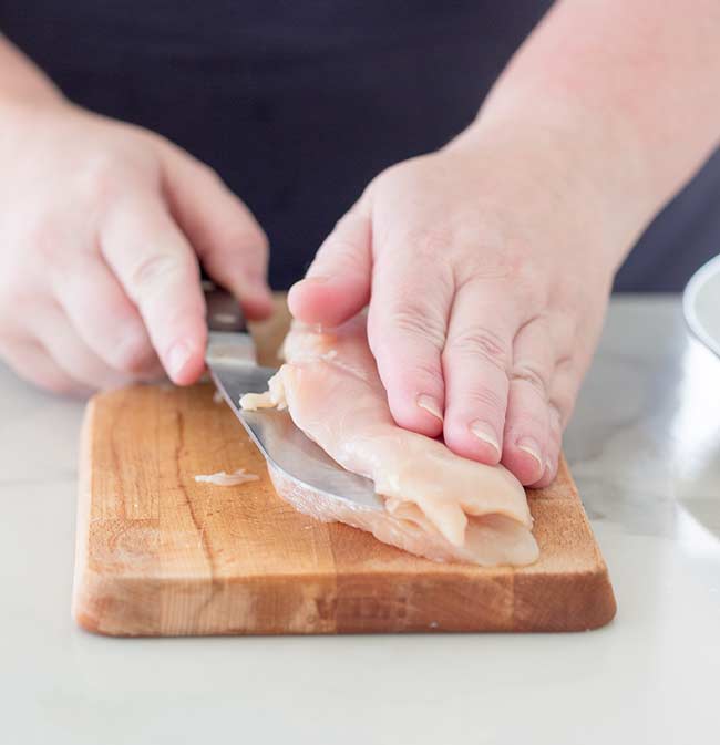 Chicken breast being filleted on a wooden chopping board
