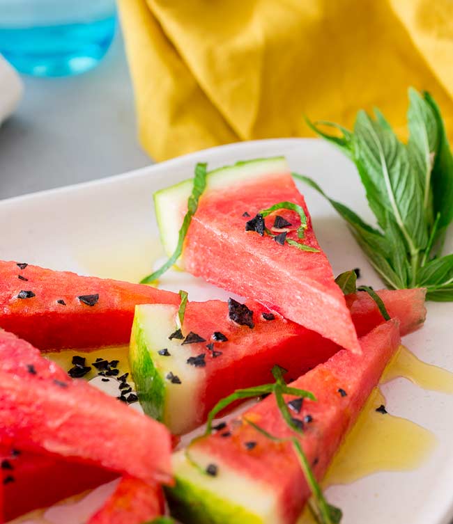Wedges of watermelon with black salt, on a white plate garnished with shredded mint.