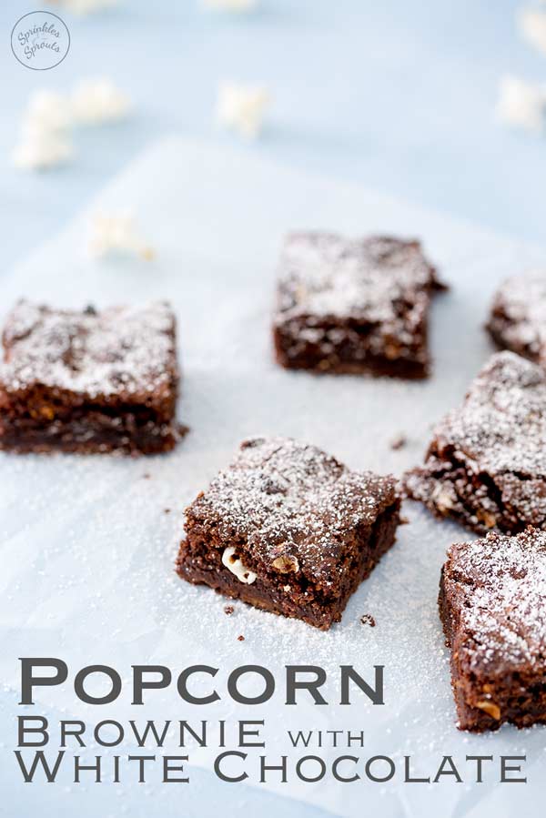 Pinterest image, 6 popcorn brownies on a sheet of parchment paper on a blue table, text at the bottom of the image