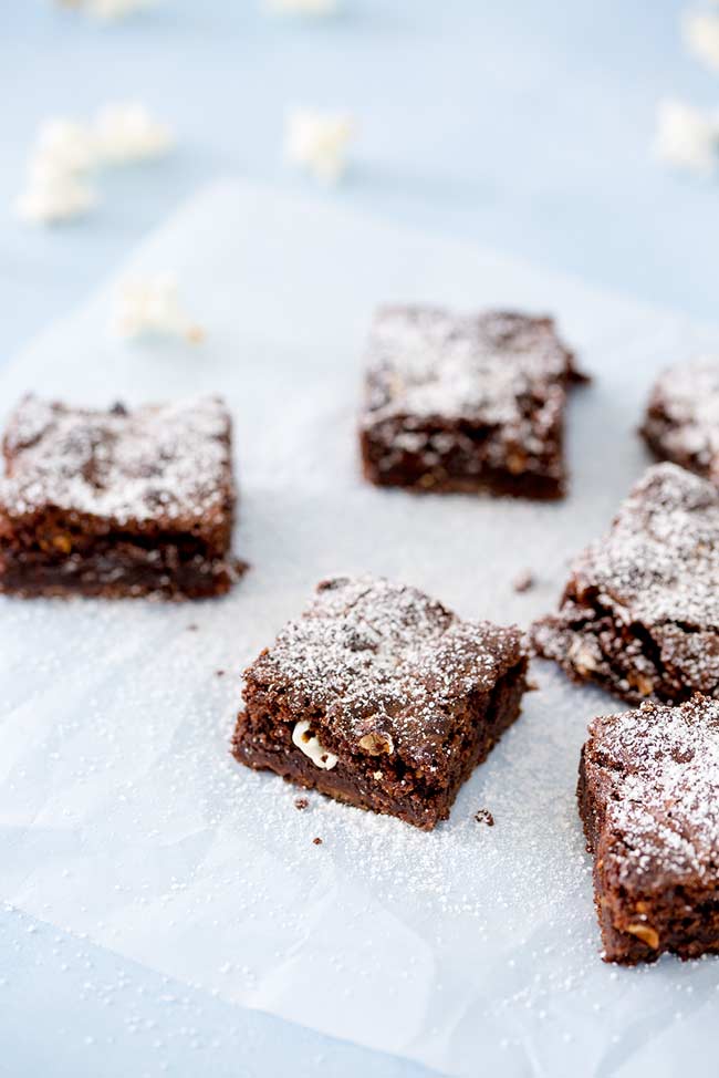 Popcorn Brownie squares, dusted with sugar, sitting on parchment with popcorn scattered around.