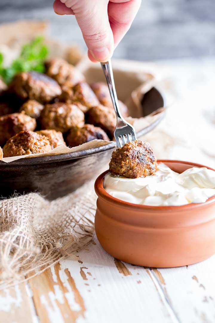 Paprika meatball on a mini fork being dipped into a terracotta pot of sour cream