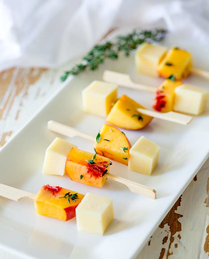 6 gouda and peach skewers on a long white plate with a garnish of fresh thyme at the back