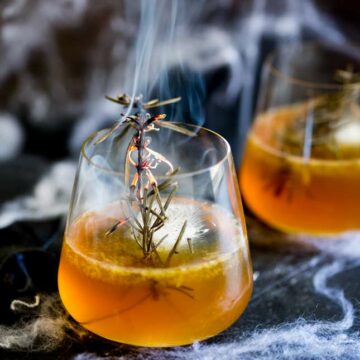 close up on a smoking sprig of rosemary in a bourbon cocktail