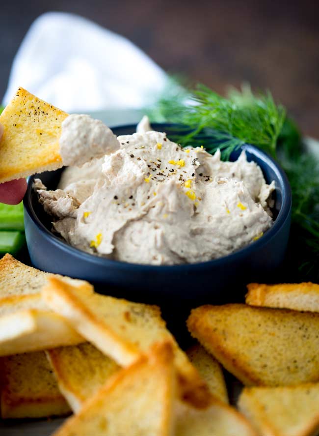 Toast point being dipped into a blue bowl of smoked fish dip