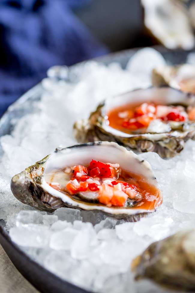 close up on an oyster sat on crushed ice dressed with a strawberry mignonette