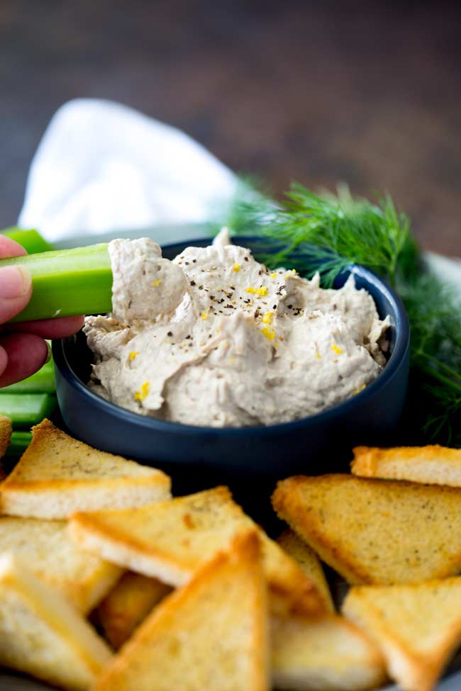 Blue bowl of smoked fish dip with a celery baton being dipped into it