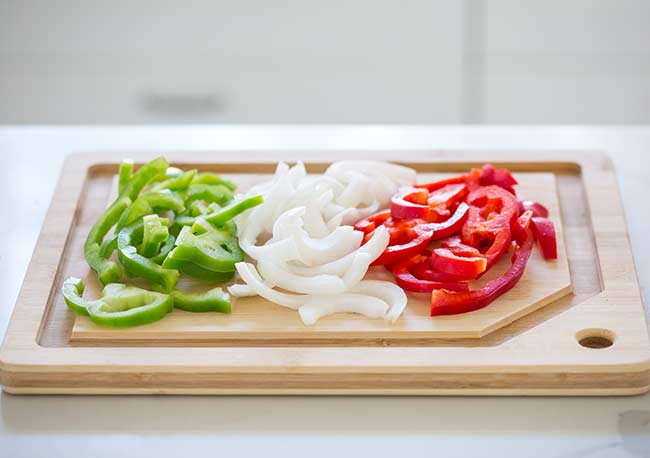slices of green bell pepper, white onion and red bell pepper on a wooden chopping board