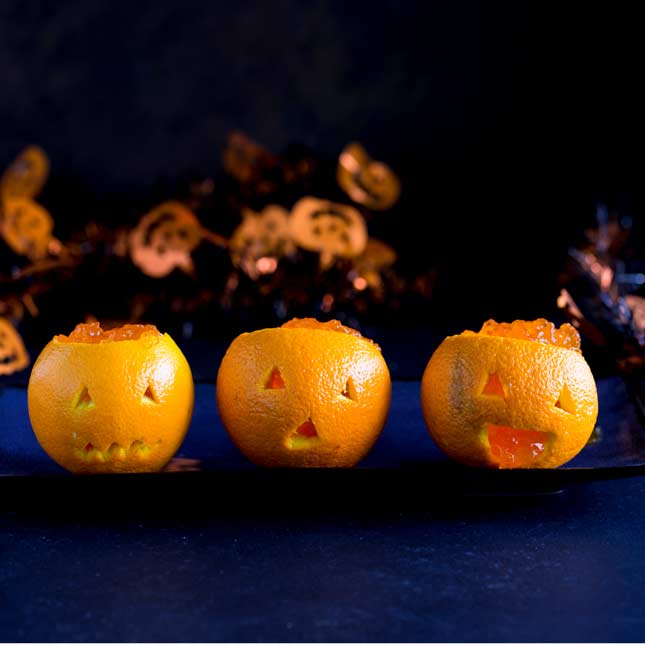 3 jack o lantern oranges sat on a blue plate on a dark table with halloween tinsel behind them