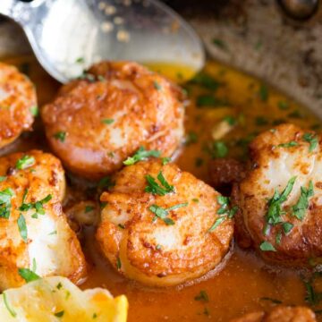 small Sq picture showing golden seared scallops in a silver pan of paprika butter with a garnish of lemon and parsley